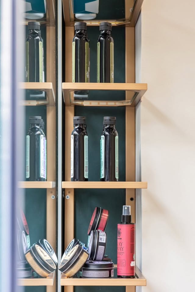 Η γυάλινη προθήκη του Barber's Chair με τα προϊόντα περιποίησης σε ξύλινα ράφια