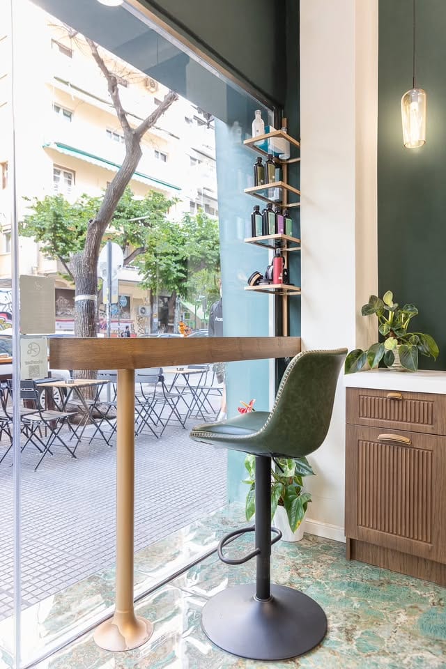 Η θέση στην τζαμαρία του Barber's Chair: ξύλινος πάγκος, πράσινο δερμάτινο σκαμπό και ο δρόμος έξω