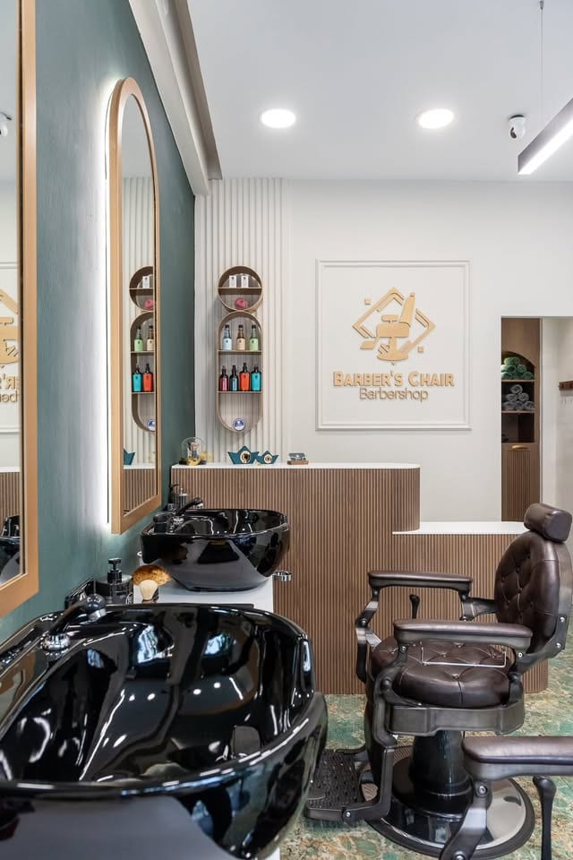 Ο πράσινος τοίχος του Barber's Chair με τον καθρέφτη σε καμάρα, το χρυσό σήμα πάνω από τον πάγκο υποδοχής και το πράσινο δάπεδο